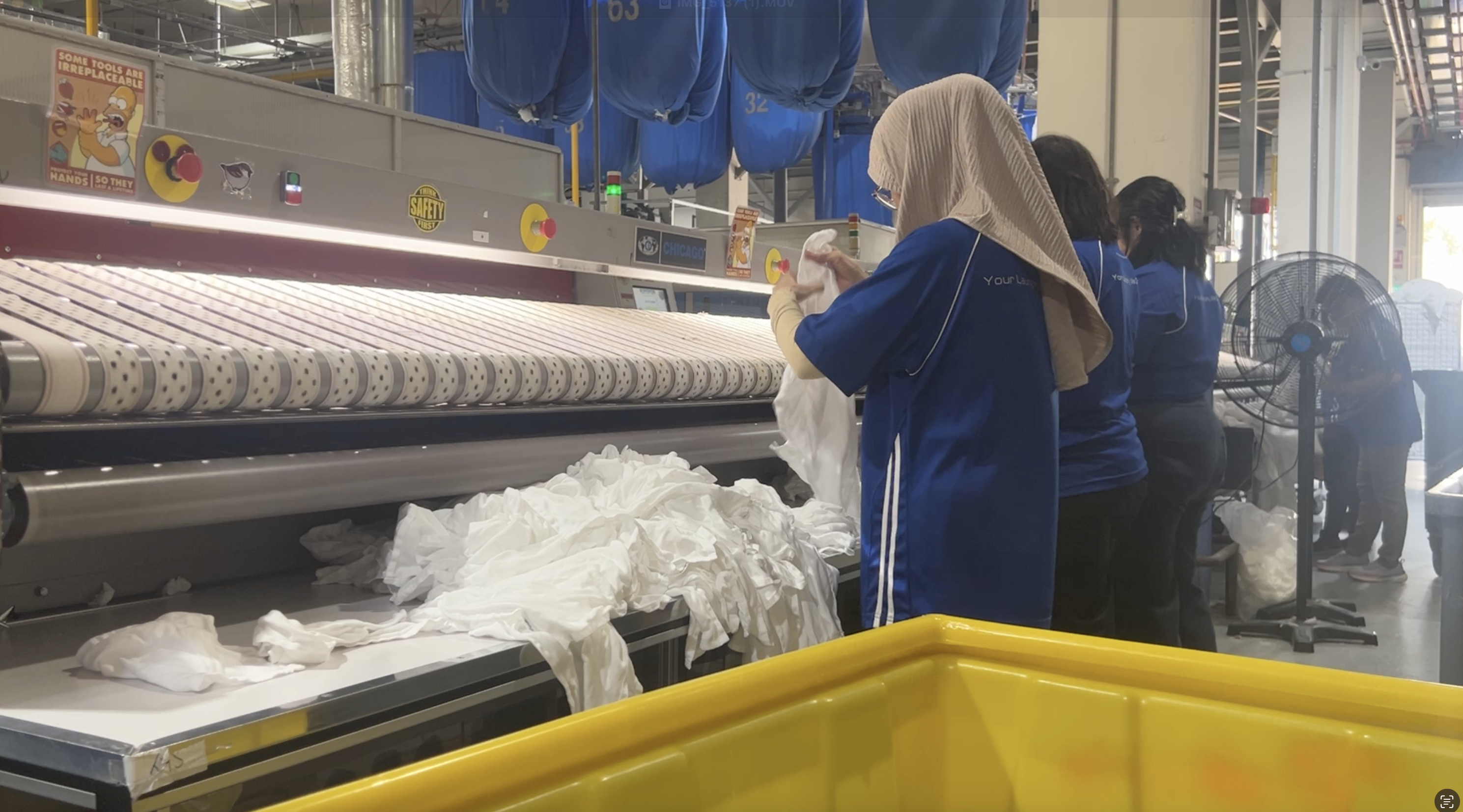 Workers performing high-volume industrial ironing inside a Singapore laundry factory.